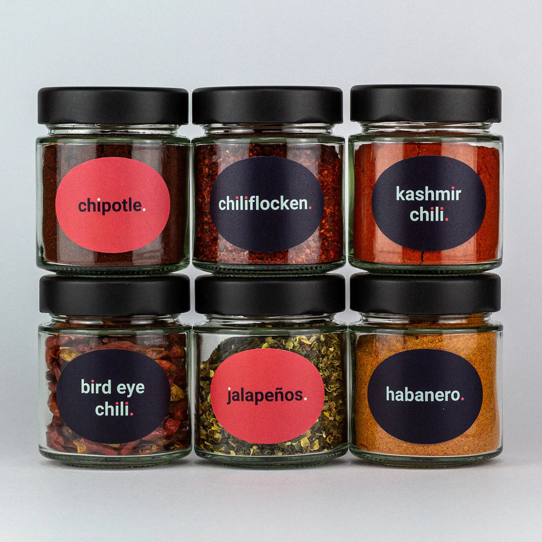 Die Gewürze des Chili SetChipotle, Chiliflocken, Kashmir Chili, Bird Eye Chili, Jalapenos und Habanero in Gläsern aufeinandergestapelt.