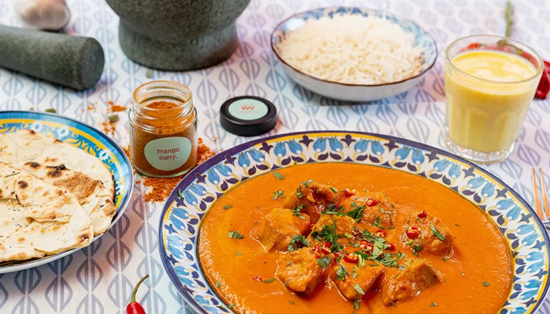 Das Kategoriebild für Curry & Masala. Zu sehen ist das Mango Curry Gewürz neben einer Portion Butterchicken mit Reis und Naan Brot.