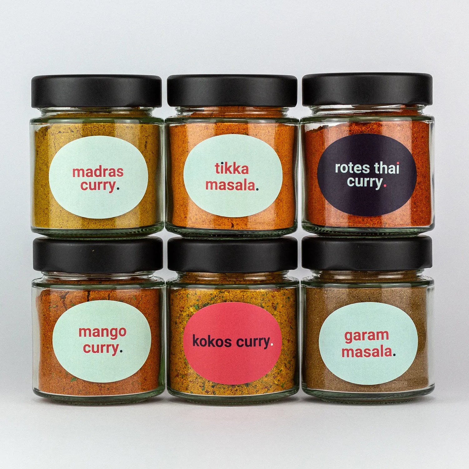Die Gewürze des Curry und Masala Set Madras Curry, Tikka Masala, Rotes Thai Curry, Mango Curry, Kokos Curry und Garam Masala in Gläsern aufeinandergestapelt.