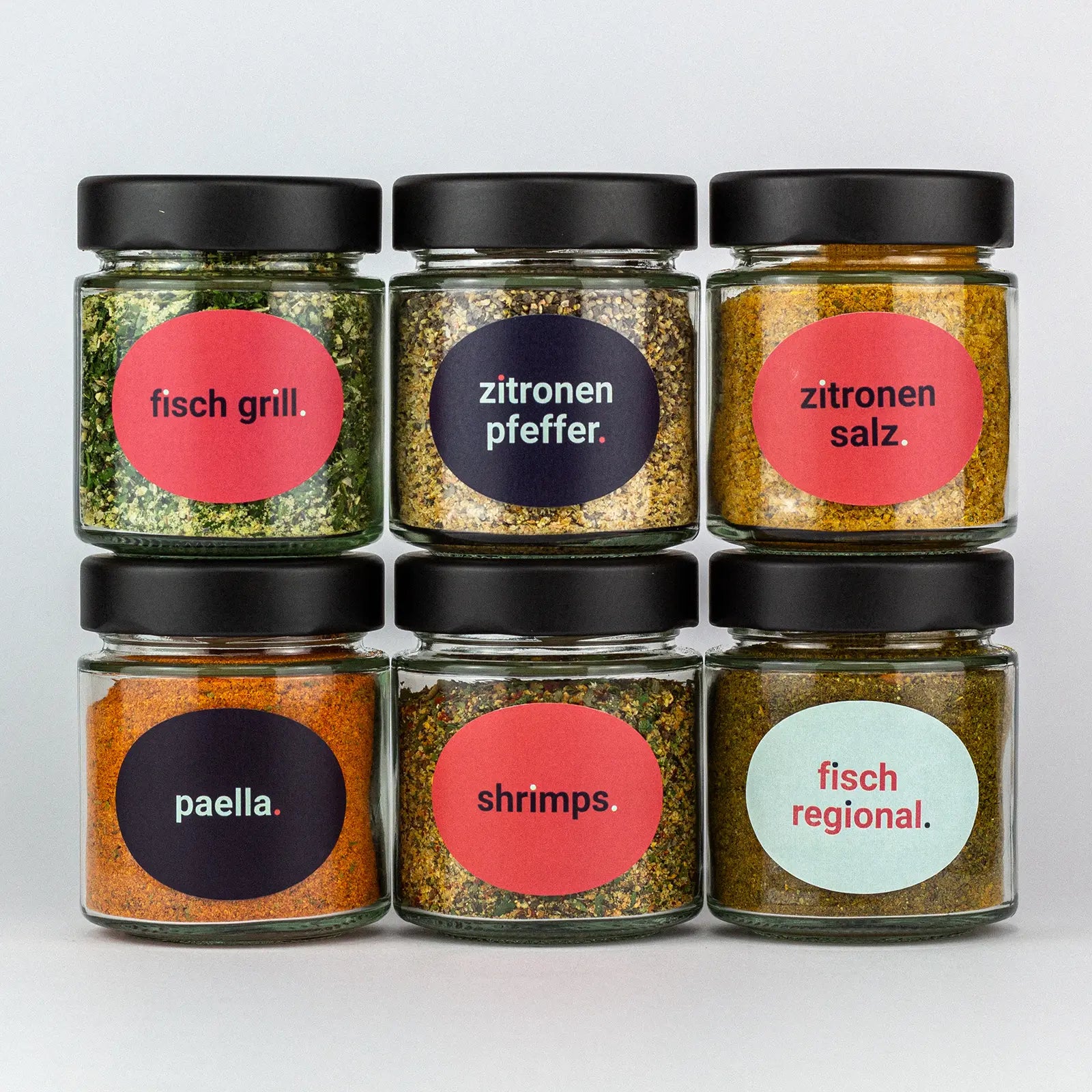 Die Gewürze des Fisch und Friends Set Fisch Grill, Zitronenpfeffer, Zitronensalz, Paella, Shrimps und Fisch Regional in Gläsern aufeinandergestapelt.