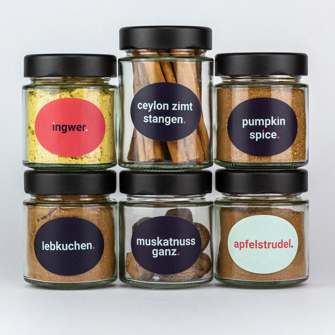 Die Gewürze des Kaffe und Kuchen Set Ingwer, Ceylonzimt Stangen, Pumpkin Spice, Lebkuchen, Muskatnuss ganz und Apfelstrudel in Gläsern aufeinandergestapelt.