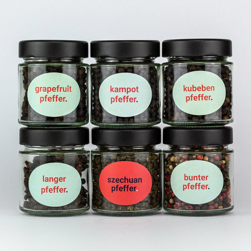 Die Gewürze des Pfeffer Set Grapefruitpfeffer, Kampotpfeffer, Kubebenpfeffer, Langer Pfeffer, Szechuanpfeffer und Bunter Pfeffer in Gläsern aufeinandergestapelt.