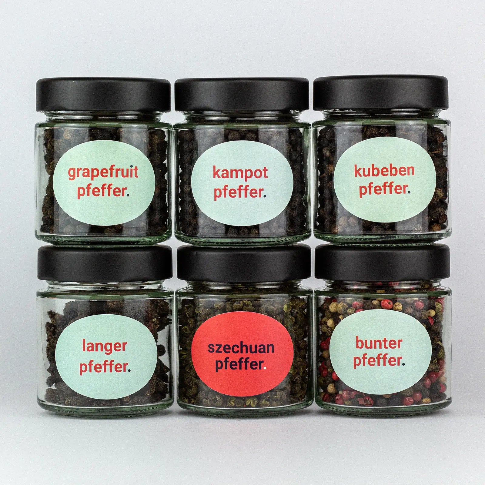 Die Gewürze des Pfeffer Set Grapefruitpfeffer, Kampotpfeffer, Kubebenpfeffer, Langer Pfeffer, Szechuanpfeffer und Bunter Pfeffer in Gläsern aufeinandergestapelt.