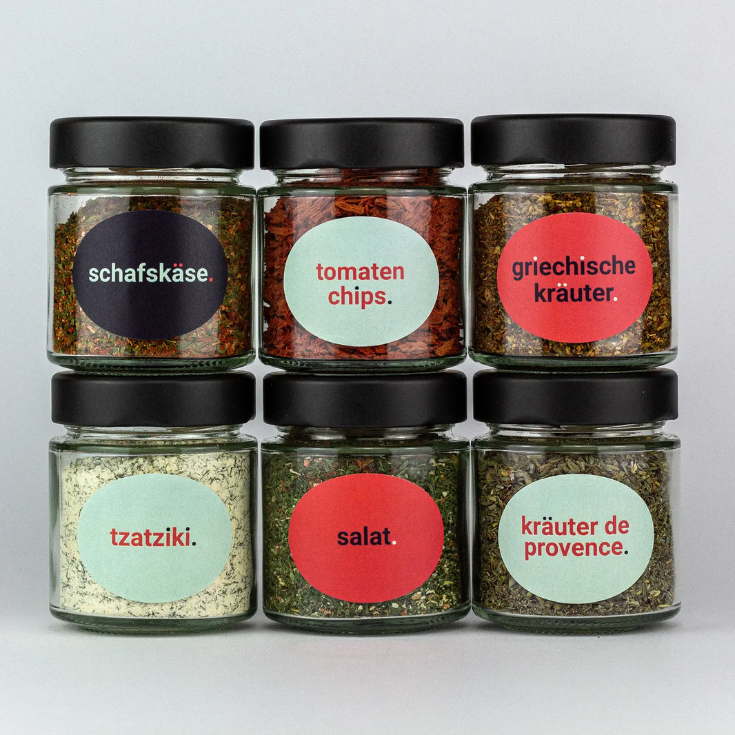 Die Gewürze des Salate und Toppings Set Schafskäse, Tomatenchips, Griechische Kräuter, Tzatziki, Salat und Kräuter de Provence in Gläsern aufeinandergestapelt.