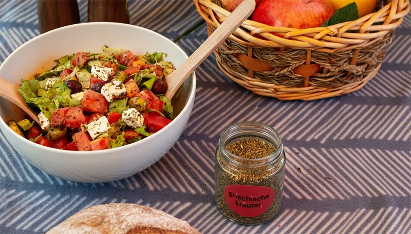 Das Kategoriebild für Salate und Toppings. Zu sehen ist das Griechische Kräuter Gewürz neben einer Salatschüssel mit Oliven, Feta und Tomaten.